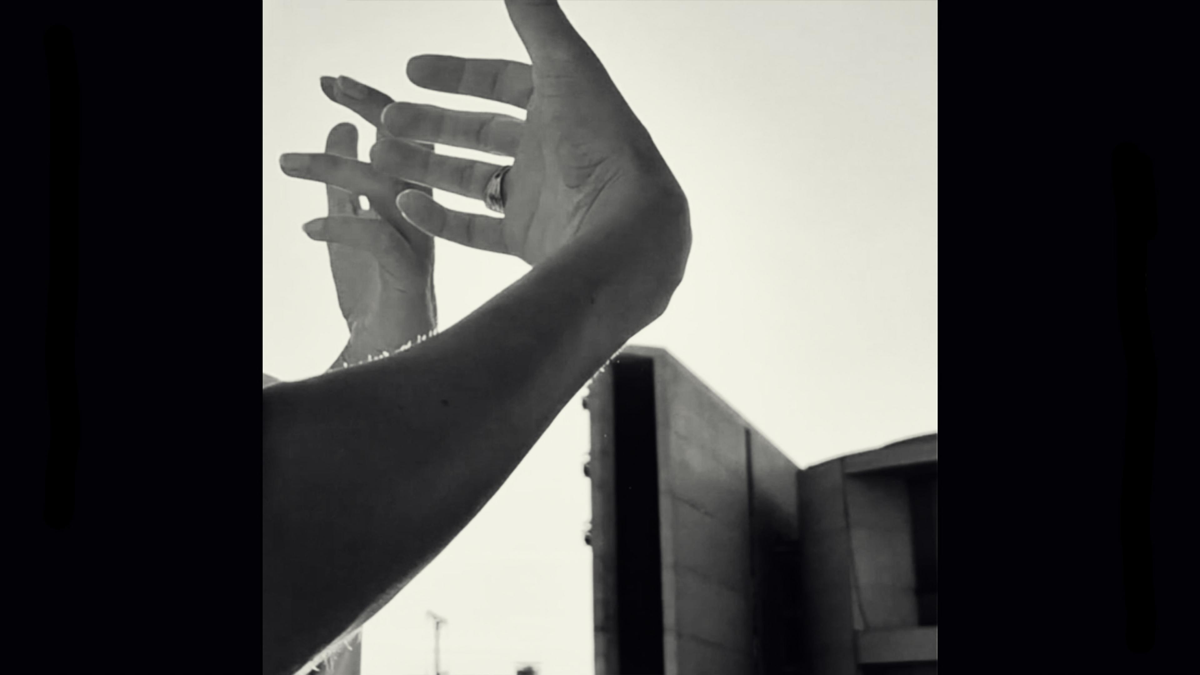 Black-and-white photo of hands framing the sky with a modern building in the background.