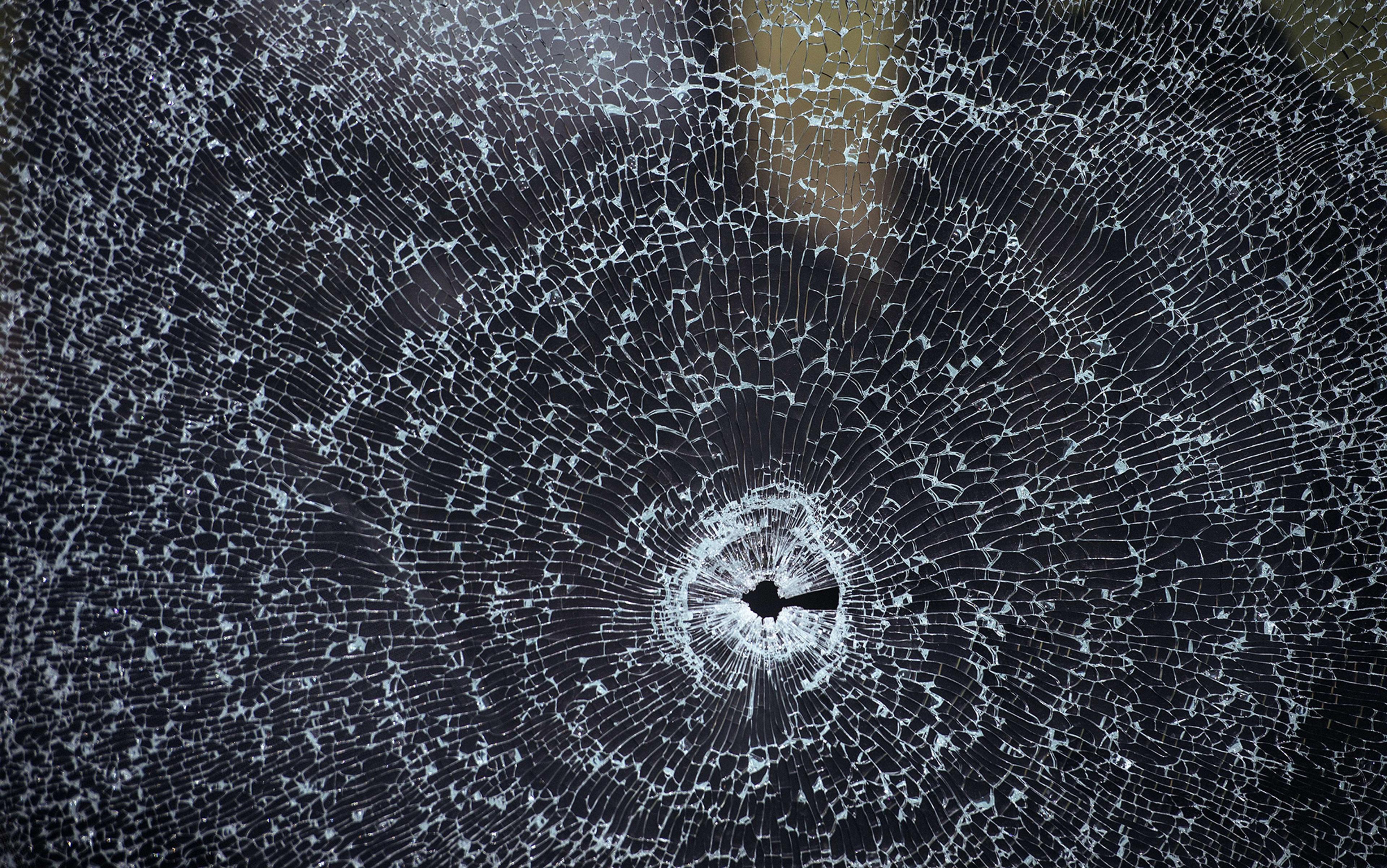 Shattered glass with a bullet hole at the centre, creating radial cracks and a web-like pattern on a dark background.