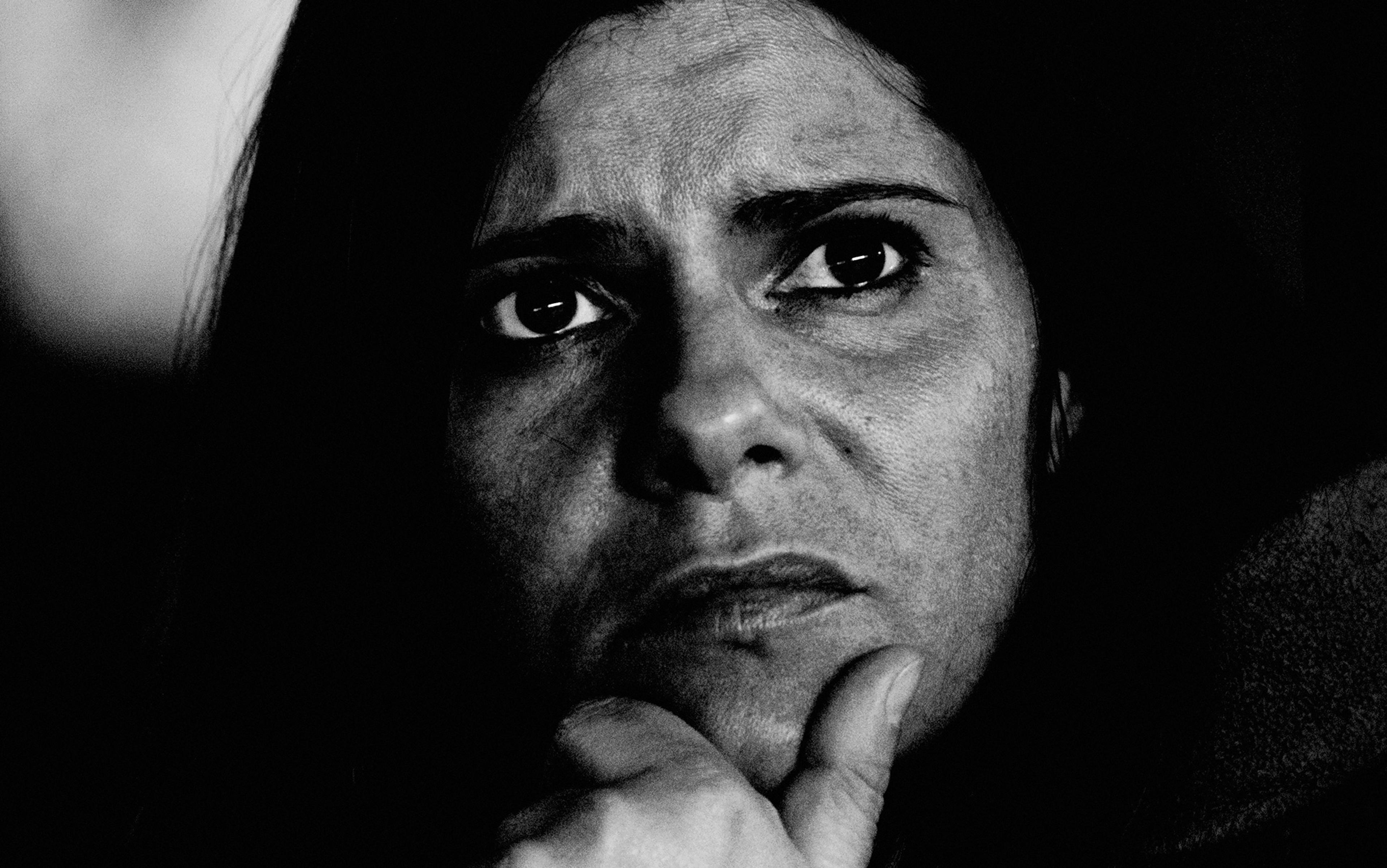 Black and white close-up of a woman with a serious expression, holding her hand to her chin, looking into the distance.