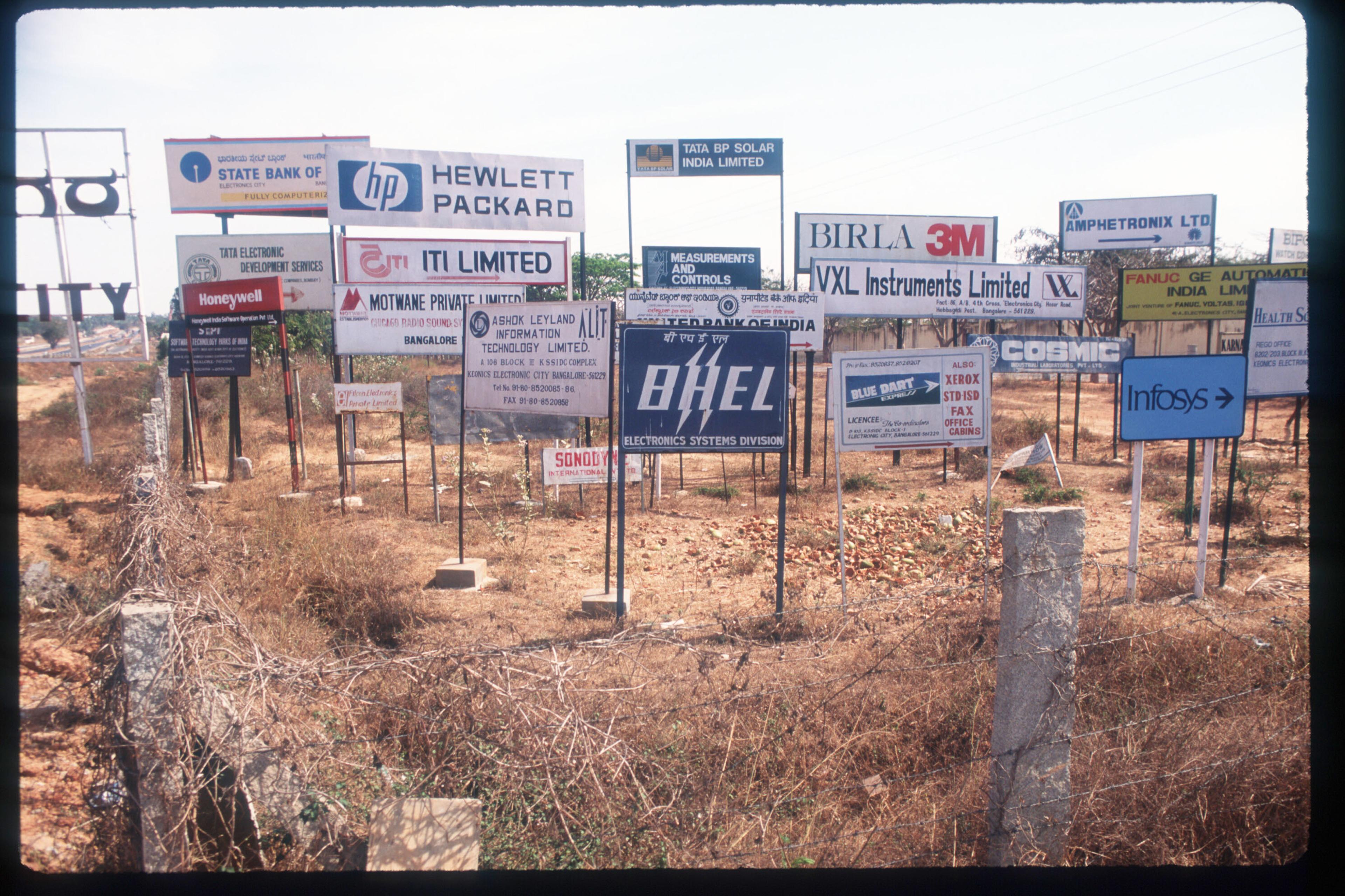A field of dry grass cluttered with computer company signboards.