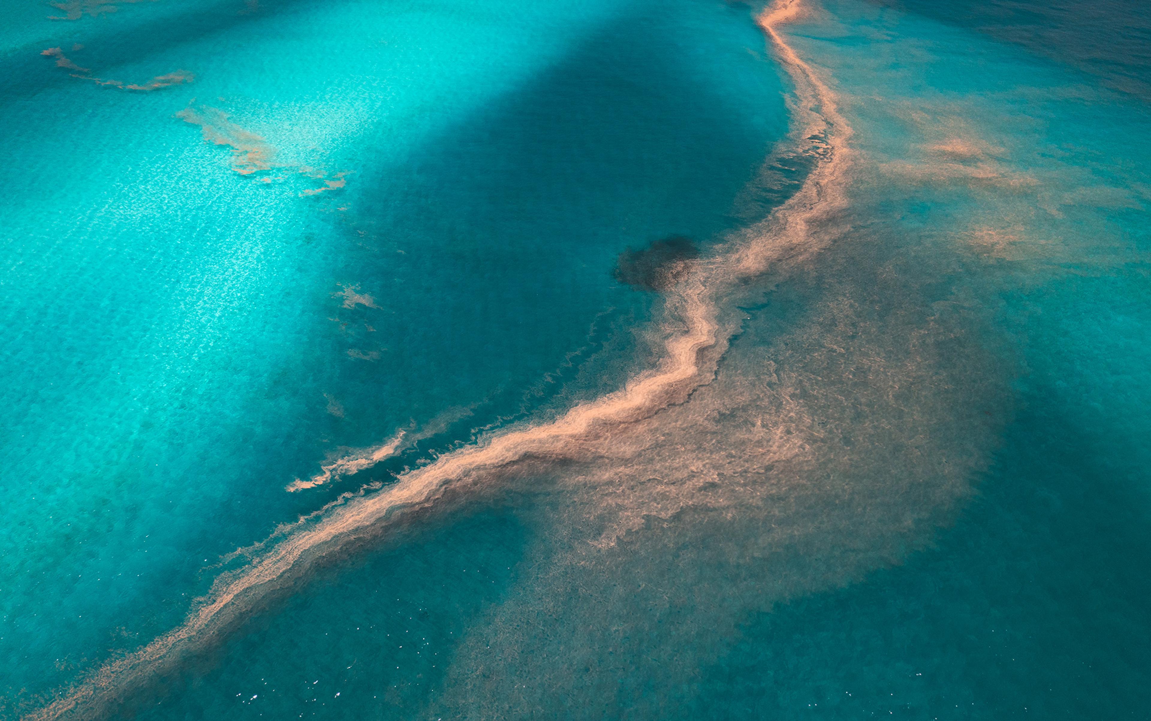 Aerial photo of turquoise ocean with a sinuous sand-coloured formation running diagonally, creating a striking contrast.