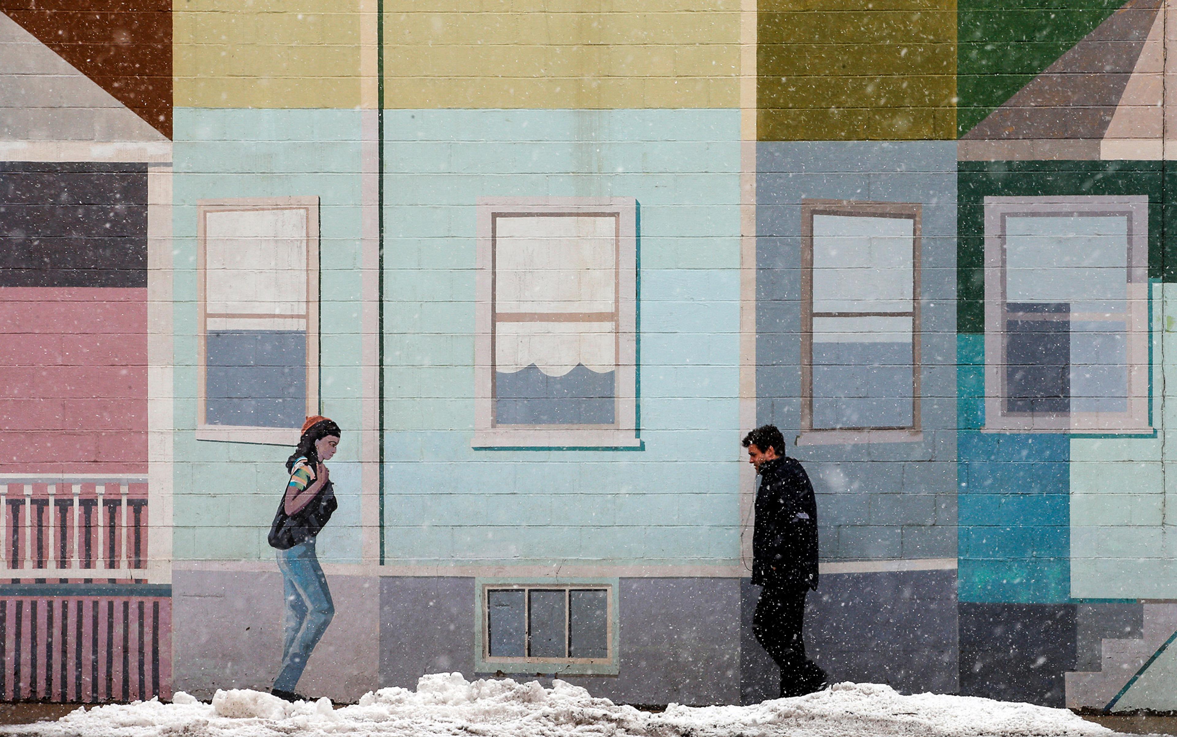 A mural depicting houses and a woman, with a man walking in front; snow is falling, and there’s snow on the ground.