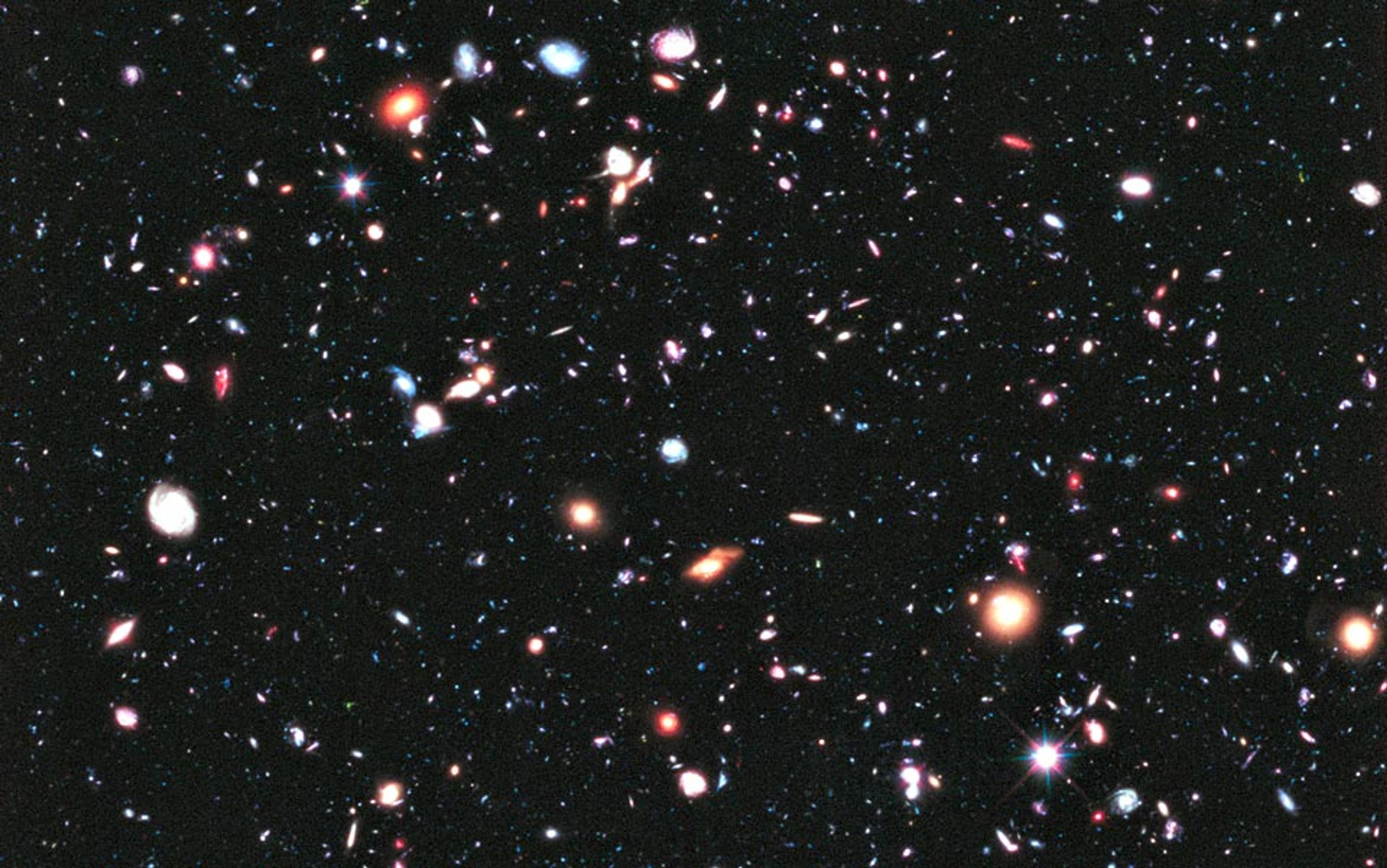Deep space showing a multitude of galaxies and stars of various colours and sizes scattered across a black background.