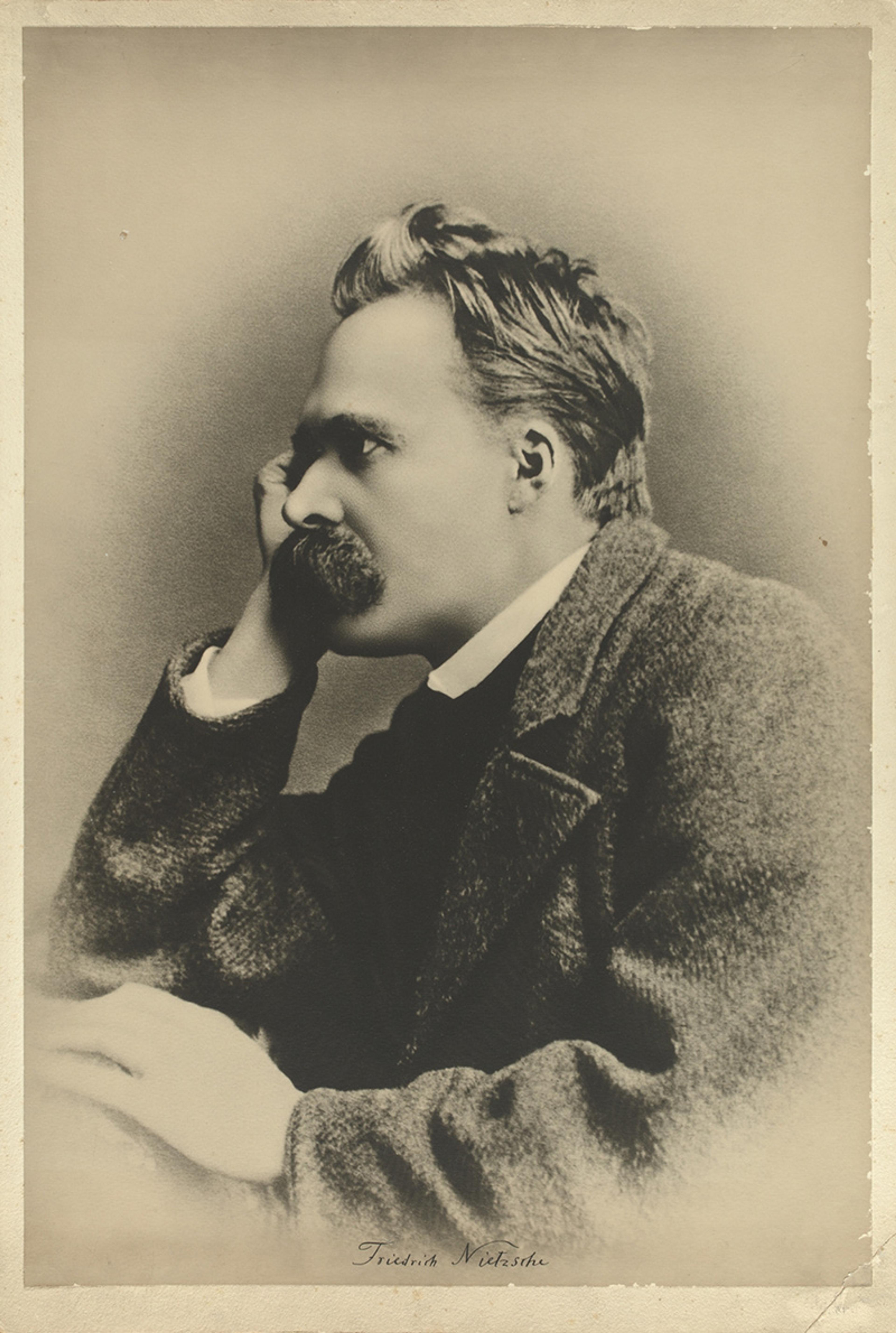 Sepia-toned photo of a man in profile with a moustache resting his head on his hand, wearing a dark coat.