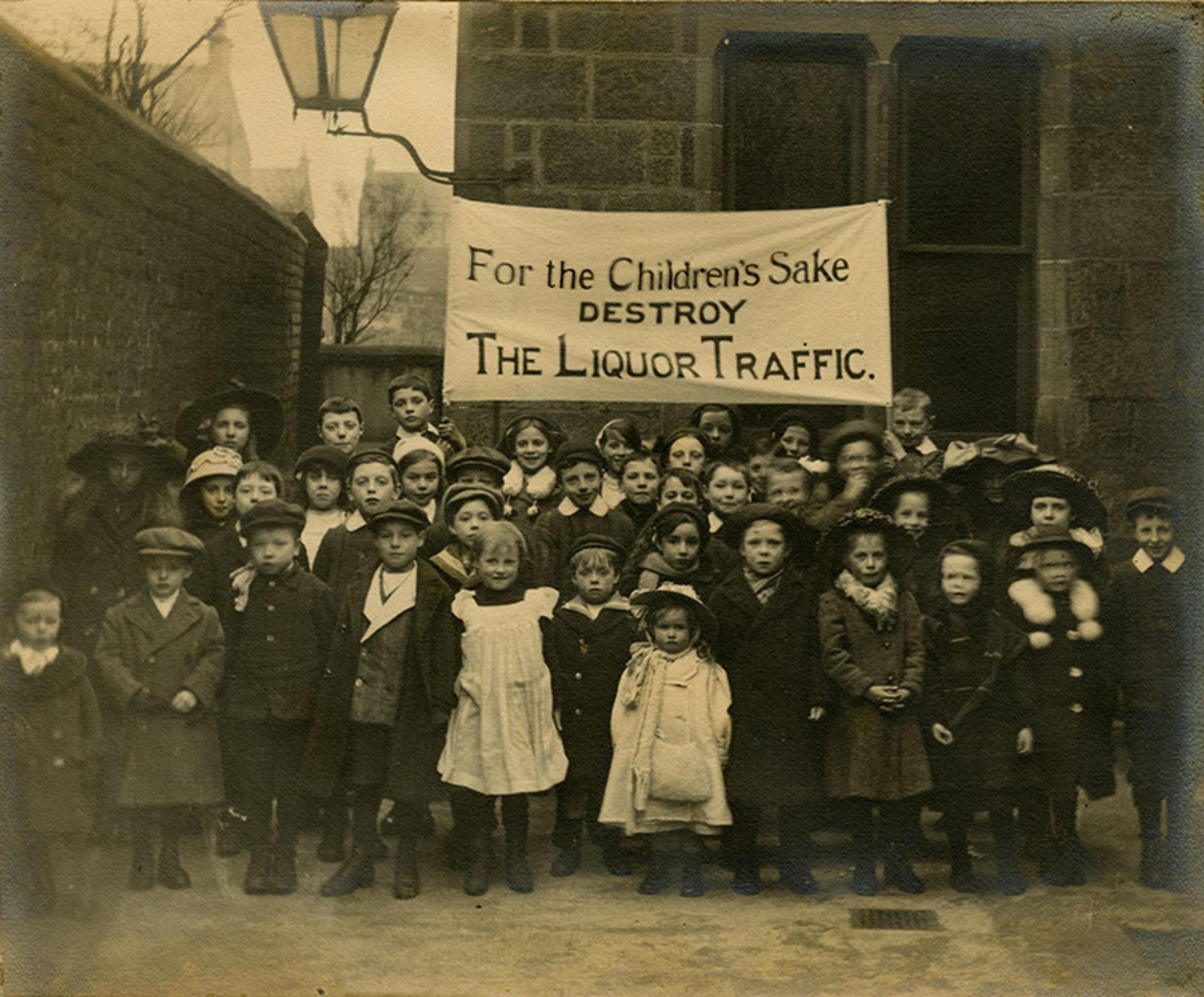 Vintage photo of children standing under a banner reading “For the Children’s Sake Destroy the Liquor Traffic.”