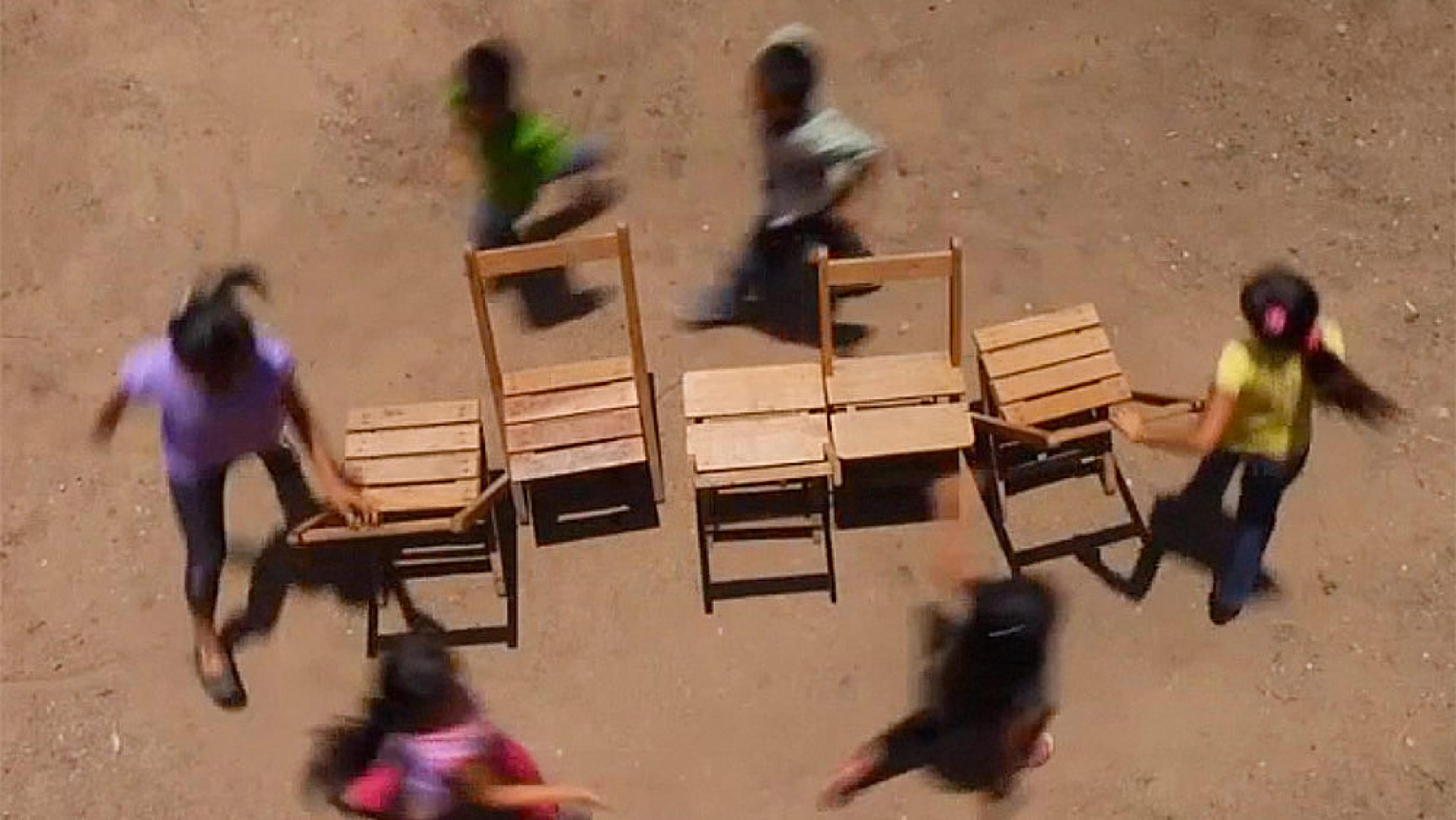 Children playing musical chairs outside. The image captures motion blur as they run around a circle of chairs.