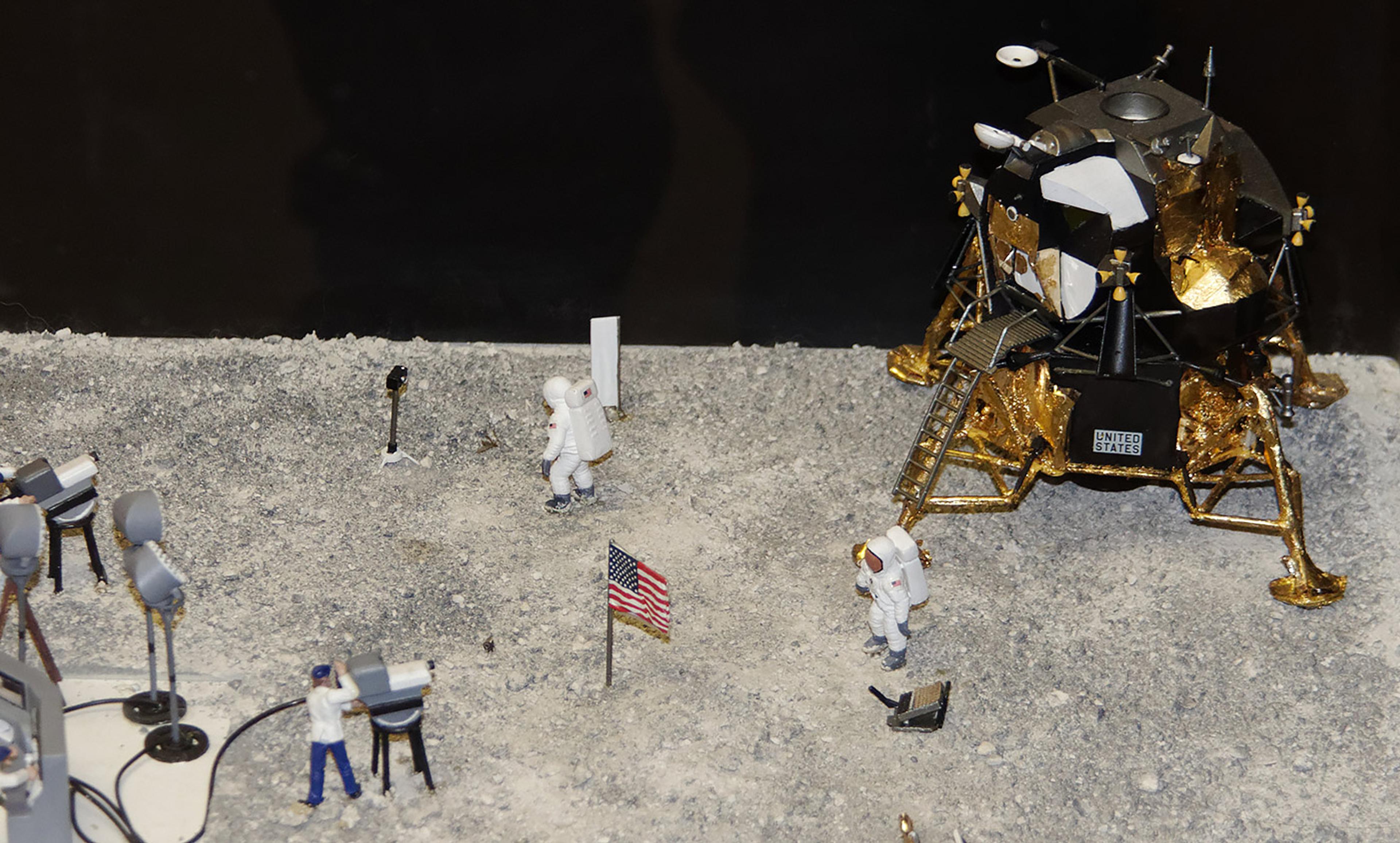Diorama depicting astronauts on the Moon’s surface with a lunar module, US flag and filming crew under studio lights.