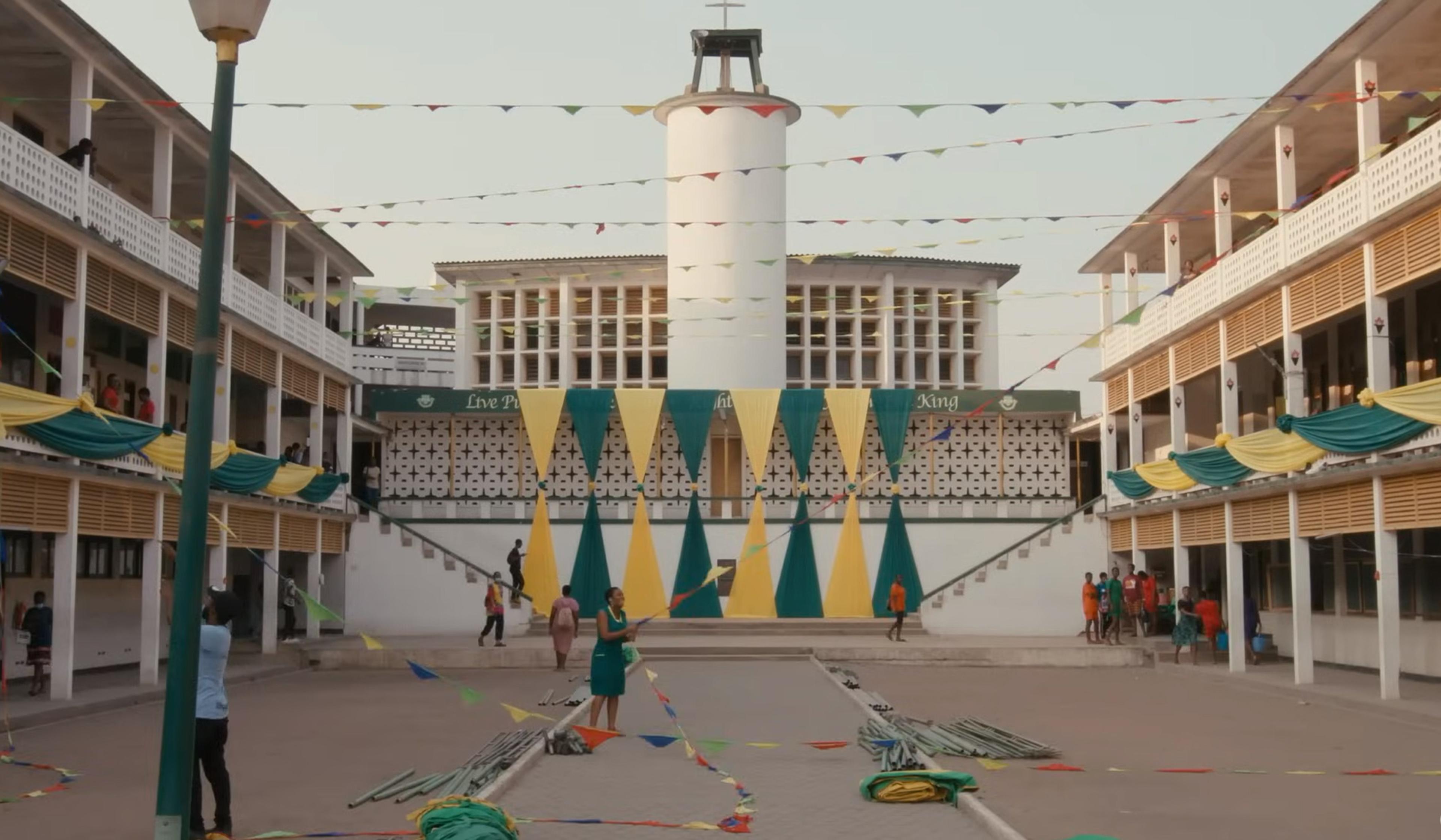 People decorating a school courtyard with green and yellow bunting.